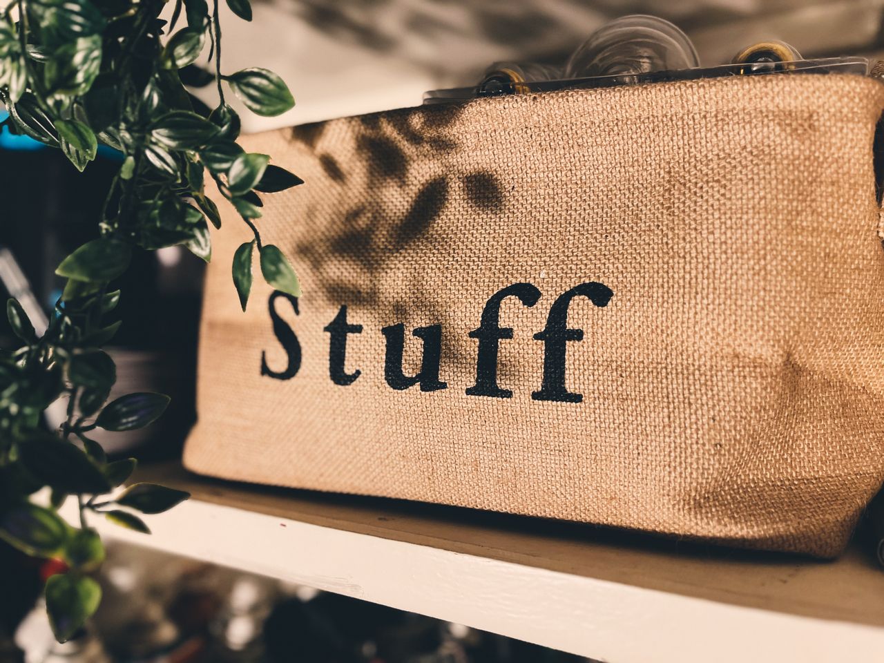 our-story Close-up of a burlap bag labeled Stuff on a wooden shelf with plants.